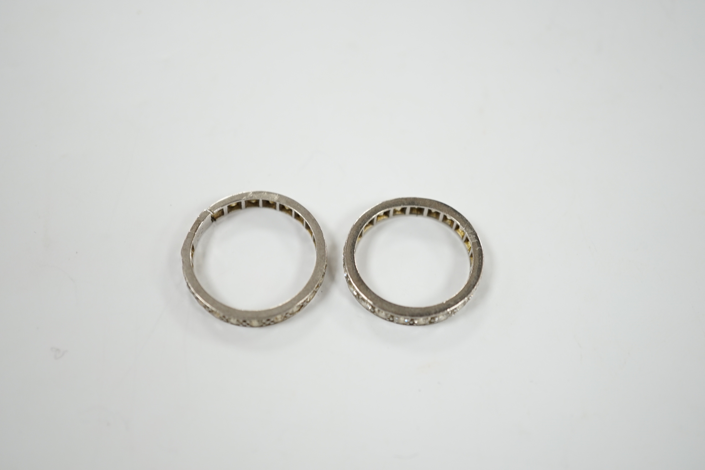 Two white metal and diamond set full eternity rings, one with cut shank and stone missing, sizes L & P, gross weight 7.7 grams.